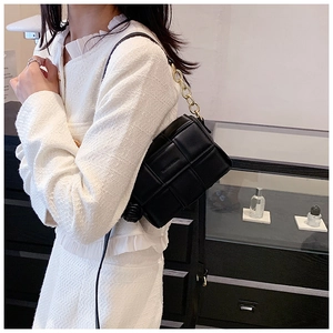 Détail d'un sac bandoulière en cuir noir matelassé avec une chaîne dorée épaisse