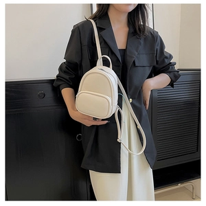 Detail of a creamy white mini backpack featuring slim adjustable straps and front zip pocket