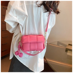 Détail du sac bandoulière carré tressé rose avec chaîne dorée et nœud décoratif