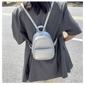 Outdoor shot of a silver-grey mini PU leather backpack with a front zipper pocket