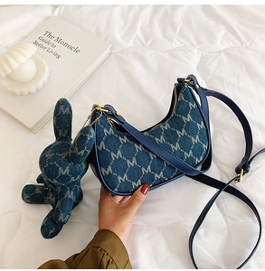 Détail du sac croissant en jean bleu avec jacquard de lettres et pendentif lapin