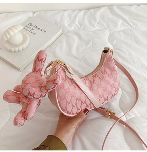 Détail du sac lune rose avec motif en M et breloque lapin sur une literie blanche matelassée