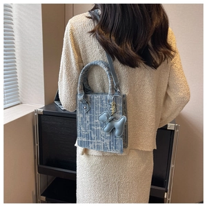 Blue and beige woven tote bag with cute dog charm worn by model as a crossbody bag