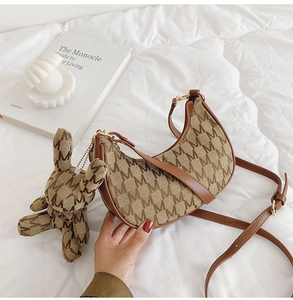Détail du sac croissant en toile avec motif monogramme et breloque lapin sur lit blanc