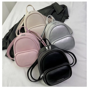 Multiple mini fashion backpacks in black, pink, beige, and silver colors on leather background