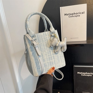 Light blue woven tweed handbag with puppy charm and leather strap in lifestyle setting