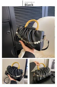 Détail du sac nuage plissé noir avec anse jaune, chaîne dorée et breloques de fleurs en perles