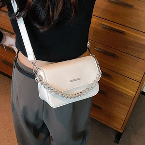 Chic cream crossbody bag with leather texture, chain strap, and metal detail on wood base