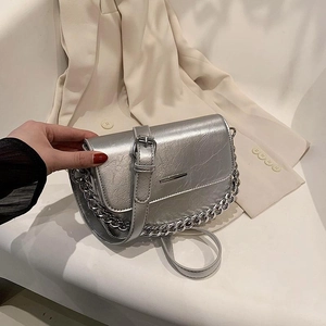 Silver metallic crossbody bag with chunky chain strap over a beige blazer backdrop
