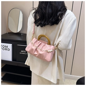 Sac nuage rose avec poignée en bois et chaîne de perles porté sur un blazer blanc chic
