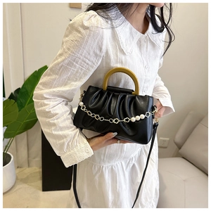 Détail du sac à plis noir avec chaîne de fleurs en perles et poignée jaune moutarde