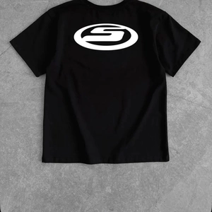 Y2K oversized black cotton T-shirt with large white S-logo print on back, flat lay view