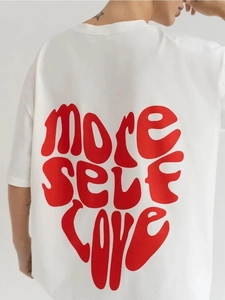 Dettaglio della stampa rossa More Self Love a forma di cuore su t-shirt in cotone bianco