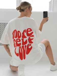Dettaglio della stampa rossa 'MORE SELF LOVE' sulla maglietta bianca in cotone oversize