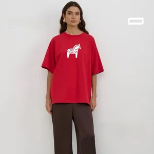 Close-up of oversize red cotton T-shirt featuring a white Dala Horse print and brown trousers