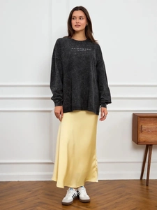 Close-up of washed black oversized sweatshirt paired with a yellow satin midi skirt