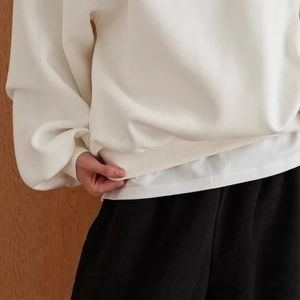Minimalist thick white crewneck sweatshirt styled with layered white tee and black trousers