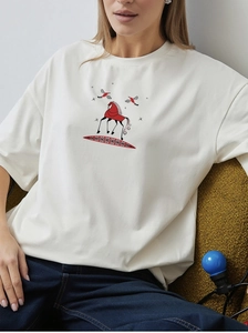 Detail of red horse print on oversized white cotton T-shirt worn by model on sofa