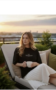 Détail du t-shirt en coton imprimé mood Prosecco et de la jupe plissée sur un balcon