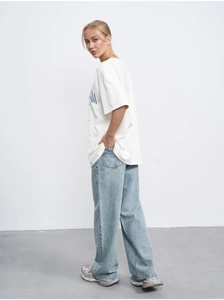 Detailed side view of a white cotton t-shirt featuring blue letter print and baggy jeans
