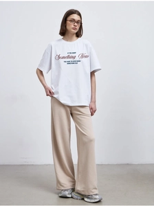 Close-up detail of white cotton t-shirt with red slogan and beige loose trousers