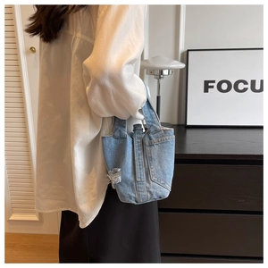Détail du sac seau en jean bleu avec finition usée et surpiqûres jaunes porté par le modèle