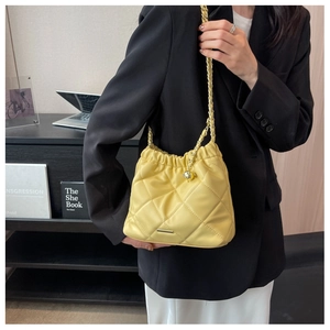 Close-up of a bright yellow quilted bucket bag with chain strap and gold plaque detail