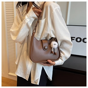 Close-up of brown leather half-moon bag featuring a decorative round buckle and plush charm