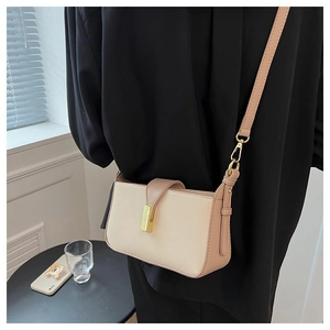 Détail d'un sac à bandoulière beige avec fermoir doré porté dans un décor contemporain