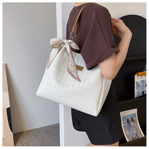 Detail of off-white quilted tote bag with brown leather strap and silk scarf decoration