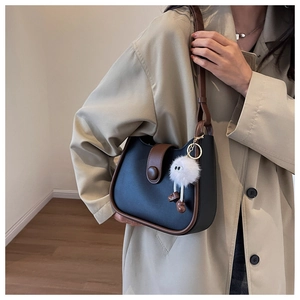 Detail of minimalist black and brown shoulder bag with a cute white plush doll pendant