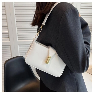 Détail d'un sac baguette en cuir blanc avec boucle dorée porté avec une veste chic