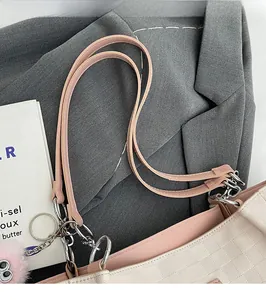 Detail of checkered tote bag with pink leather handle, silver rings, and plush charm
