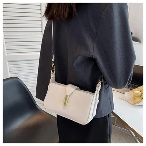 Sac bandoulière blanc minimaliste avec fermoir doré porté sur un blazer foncé