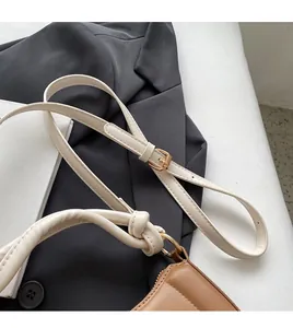 Détail de la bandoulière beige ajustable avec nœuds et boucle dorée sur un sac marron