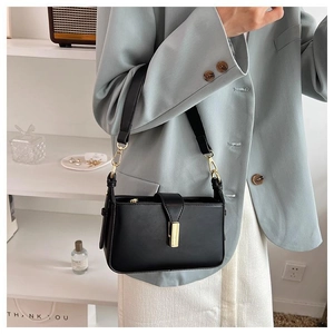 Gros plan du sac bandoulière en cuir noir avec boucle dorée porté par un mannequin