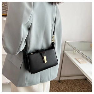 Détail d'un sac en cuir noir avec boucle dorée porté sur un blazer bleu clair