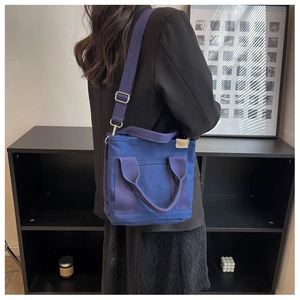 Detail of dark blue canvas tote bag featuring double handles and a wide shoulder strap