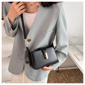 Sac bandoulière chic en cuir noir avec boucle dorée élégante porté par un mannequin en costume