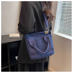 Detailed view of the dark blue canvas tote bag worn as a crossbody bag by a model