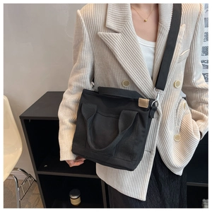 Detail of minimalist black canvas crossbody bag featuring short handles and long strap
