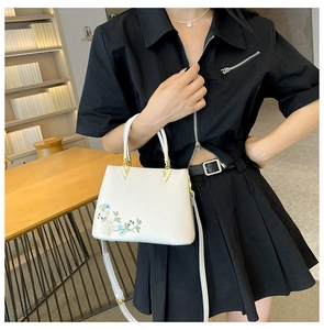 White faux leather crossbody bag with floral embroidery and gold V-shaped buckle detail
