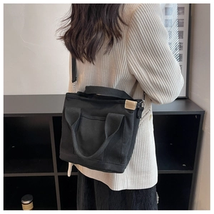 Minimalist black canvas tote bag with adjustable strap worn by model in a casual style