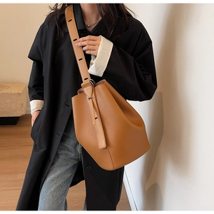 Detail of a brown grain leather bucket bag featuring a wide adjustable shoulder strap