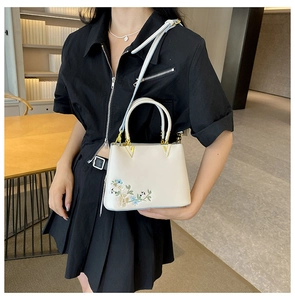 Detailed embroidery view of floral patterns and gold hardware on beige handbag