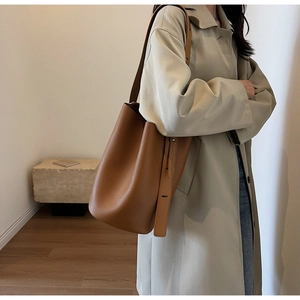 Brown leather bucket bag with wide adjustable strap worn over the shoulder by a model