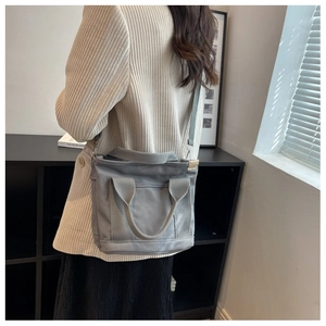 Gray canvas tote bag featuring double handles and adjustable crossbody strap on model