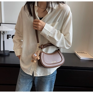 Détail d'un sac demi-lune en cuir marron avec logo doré et accessoire de charme en peluche