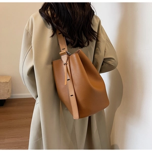 Brown litchi grain leather bucket bag with wide strap on model in trench coat