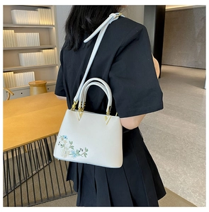 Detail of floral embroidery and gold V-shaped hardware on a beige tote bag